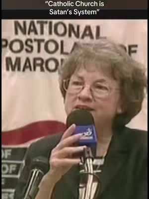A woman with glasses and gray hair speaks into a microphone. The background shows a banner, somewhat out of focus, with the words "NATIONAL APOSTOL." A text overlay at the top reads, "Catholic Church is Satan's System."