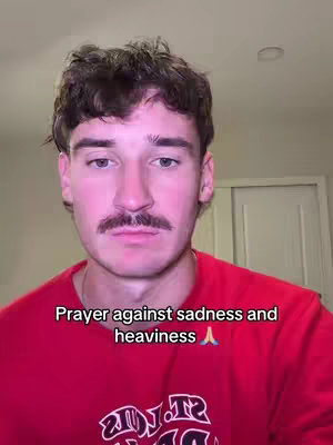 The cover image features a man with short brown hair, a mustache, and a red t-shirt. The text overlay reads 'Prayer against sadness and heaviness' with an emoji of hands in prayer.