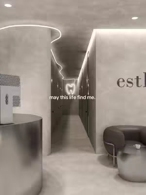 An interior shot of a modern dental clinic hallway. The hallway is long and leads to several doors. A glowing tooth-shaped sign hangs in the distance. The design is minimalist with a muted color palette.