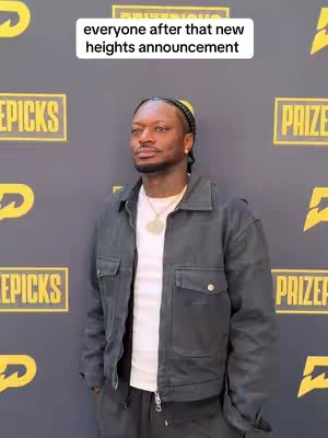 A man stands in front of a dark backdrop with yellow logos. He wears a denim jacket over a white shirt, a small gold chain, and has a serious expression. Text overlaid at the top reads 'everyone after that new heights announcement'.