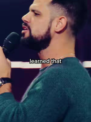 The cover image portrays a medium shot of a man speaking into a microphone. He is seen from the side, turned toward the left, with his profile visible. He has short, dark hair with a closely trimmed beard, and is wearing a green sweater. The microphone is held close to his mouth. The background is dark.