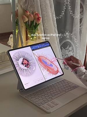 The cover image showcases an iPad set up as a laptop, viewed at a slight angle. The iPad is open, with a visible screen displaying biological diagrams. A stylus hovers over the screen. Below the iPad is a white keyboard. The background includes a floral arrangement, a mirror, and a sheer white curtain. The overall setting is bright and clean, suggesting a workspace or study area.