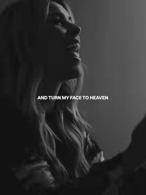 A black and white image featuring a woman with long, wavy hair, looking upwards with an expression as if she is singing or speaking passionately. Text is overlayed in a sans-serif font near the bottom, reading 'AND TURN MY FACE TO HEAVEN'. The lighting is focused, highlighting the woman's face and hair, creating a dramatic effect.