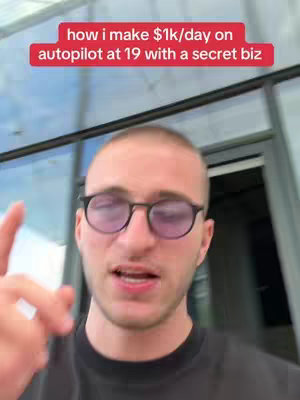 A young man with short hair and glasses is positioned in front of a glass door or window. He is looking towards the camera and gesturing with his hand.