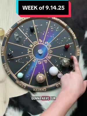 The image shows a circular board with astrological signs and gemstones, a hand points to one of the gemstones. The background includes a cow-print design. Text overlays include the date and phrase.