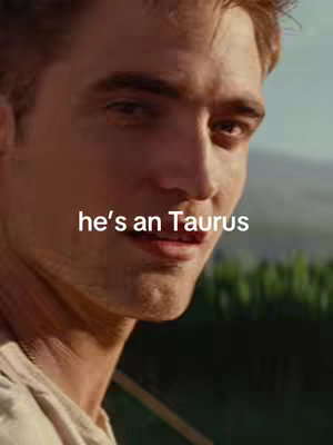 The image shows a close-up of a man's face, the right side is more visible. He has light skin, short brown hair, and is looking slightly off to the side with a contemplative expression. Overlaid text reads 'he's an Taurus'. The background shows some greenery, suggesting an outdoor setting, it's a bit out of focus.