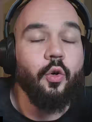 The cover image is a close-up of a man's face. He has a bald head with a thick, dark beard that frames his face. He wears headphones. His eyes are closed, and his lips are slightly pursed, giving the impression that he is concentrating or blowing air. The background is dark and out of focus.