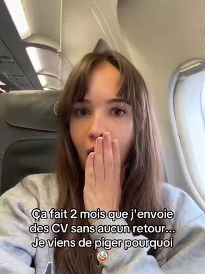 A young woman with long, brown hair and bangs is seated on an airplane, looking surprised and covering her mouth with one hand. The background shows the inside of an airplane with seats and windows. Text overlays the image, providing context.