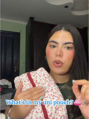 A young woman with long dark hair and fair skin is holding a floral pouch, centered in a vertical video frame. A speech bubble with text overlays the content just under her face. She is mid-sentence, looking directly forward with a soft expression. The background is a glimpse of a room, suggesting a casual setting. The color palette is bright, with pink and green tones adding to the overall aesthetic.