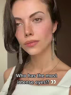 A woman with dark hair and dangling earrings stares intently at the camera.