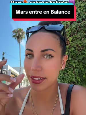 A selfie-style image features a woman with dark hair, sunglasses perched on her head, and a bright, outdoor setting. The background includes a palm tree and lush green foliage. The woman is the focus, with the overlaid text in a rectangular banner and a pink and black color scheme.