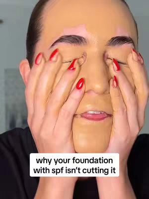 A close-up shot of a person’s face covered in foundation, with red nails, arms covering the face, and white text box at the bottom of image with text.