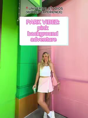 A woman stands in front of a bright pink background. She wears a white top and light pink skirt with white shoes. A sign above the woman reads, "PARK VIBEZ: pink background adventure."