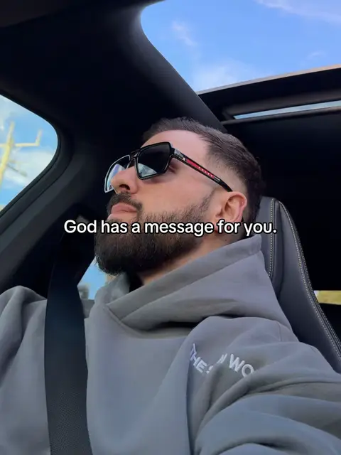 A man in sunglasses is seated in a car. The background shows a blue sky and a cityscape which provides background to the subject. The overlay text says "God has a message for you."