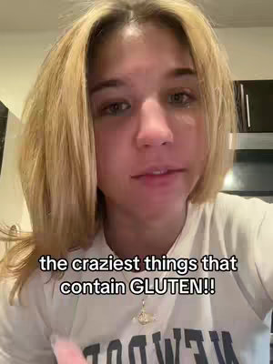 A young woman with blonde hair looks directly at the camera. The text overlay reads "the craziest things that contain GLUTEN!!". She is wearing a white t-shirt, and the background includes parts of a kitchen.