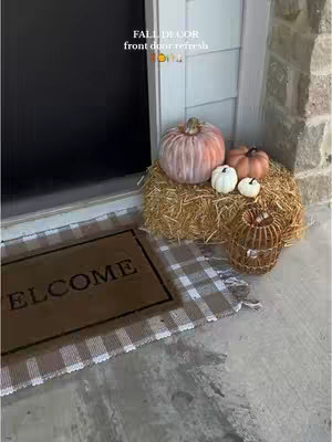 The cover image shows a decorated front door for fall. A "WELCOME" mat sits on a gray and white checkered rug. Next to the door, a bale of hay is topped with various pumpkins in shades of white, orange, and pink. A decorative wicker lantern sits on the ground. The overall color scheme is warm and autumnal.