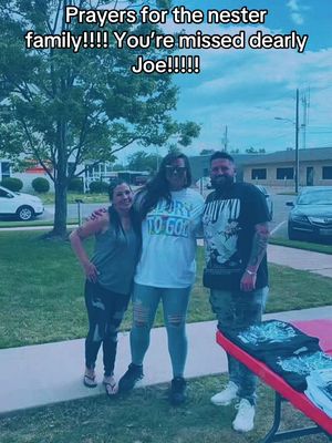 A photo of three people posing for a photo outside. They are standing on what looks like concrete. A woman on the left is wearing a gray tank top and ripped black pants. In the middle is another woman wearing ripped jeans, black boots, and a t-shirt that says "Born To God". The man on the right is wearing a black t-shirt and jeans with some tattoos on his arm. Behind them is a tree and a blue sky. The image has a slight blue tint.