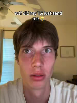 A young man with brown hair and a concerned expression is centered in frame, illuminated by a ceiling light, with text overlay on the top which expresses surprise. The background includes a window with a curtain and a wall with a framed picture.