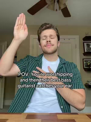 A young man with light skin and short, light brown hair, wearing a green striped shirt over a white t-shirt, raises his right hand in a gesture of worship with his eyes closed. The background consists of a muted beige wall and a ceiling fan. Black text in the style of a meme covers the lower half of the frame.