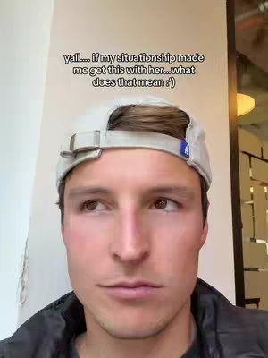 A close-up shot of a young man wearing a cap and a zipped-up jacket. He is looking off to the side, possibly thinking, while text overlays the top of the image.