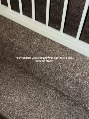 The image shows a section of a gray carpet floor and a white railing or gate in the upper part of the image. Text is overlaid at the bottom, describing toddler sleeping habits. The composition is simple, with a neutral color background.