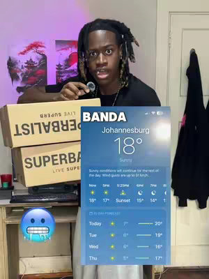 A person is shown from the chest up, holding a silver object in their mouth. They are looking at the camera with a surprised expression. In the background, there is a desk with boxes on which is written a weather widget with Johannesburg's weather information. The background shows a room setting with items like a window frame and a piece of art.