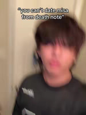 The cover image features a slightly blurred medium shot of a young man, with the focus primarily on his upper body and face. The man has short, dark hair that obscures his forehead slightly. He's wearing a black t-shirt. The background is out of focus, suggesting an indoor setting. A text overlay at the top of the image reads, 
"you can't date misa from death note."