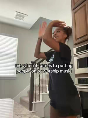 A young woman with dark skin is captured mid-dance, her arms raised as if she is celebrating. She wears a black t-shirt and shorts, her hair is pulled back in a bun. The image is taken indoors, against a background that includes a staircase and neutral colored walls and cabinets. White text is added to the cover, describing the content of the video.
