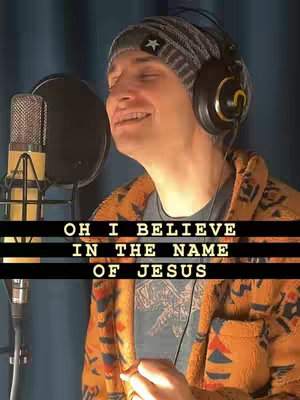A man wearing a beanie and headphones sings into a microphone with text overlayed on the image.