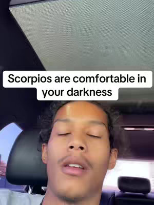 The cover image shows a selfie-style shot taken from inside a car, with the person facing the camera. The background appears to be the car's interior, including the ceiling and a portion of the visible surroundings outside. The person is a young man with curly hair and wearing a dark shirt. Above his face, a white rectangular text overlay reads, 'Scorpios are comfortable in your darkness'. The lighting suggests the car is partially shaded, with the person's face lit by the sun.