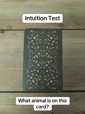 The image shows a vertical shot of a wooden surface, likely planks of wood. Overlaying this is a dark green rectangular playing card with a floral or ornate pattern. Above the card is a white rectangle with the text 'Intuition Test,' and below the card is another white rectangle containing 'What animal is on this card?'