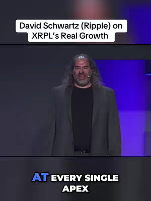 A vertical video screenshot featuring David Schwartz, a man with long gray hair, wearing a dark suit and black undershirt, speaking at a conference. The background is composed of a dark stage with purple and blue lighting. Text overlays provide context.
