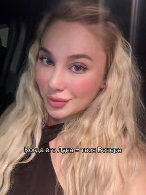 A selfie-style shot featuring a woman with long, wavy blonde hair and blue eyes. She has a light complexion and is wearing some makeup, including pink blush. The text overlay reads, "Когда его Луна = твоя Венера", which is in the Russian language.