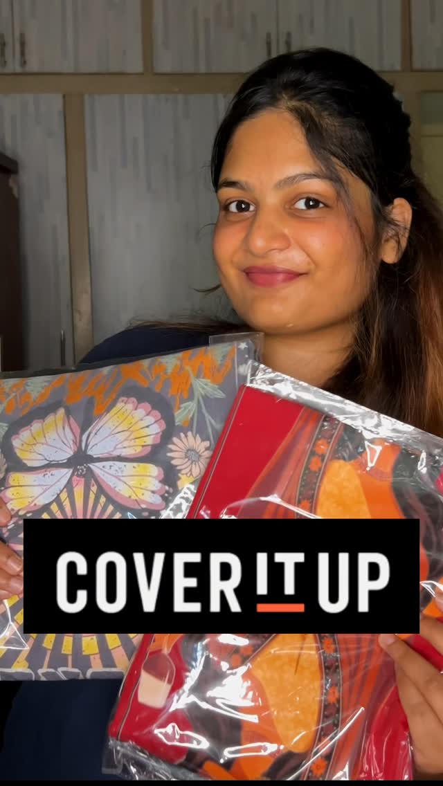 A woman is holding up three sealed plastic packages with designs, showcasing them towards the camera. She's smiling. A black rectangular bar at the bottom has the text "COVER IT UP" in white, centered. The background is a blurred indoor setting.