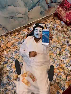 A person wearing a white mask with a mustache and a white robe is lying on a bed of money, holding a phone displaying a trading app. The phone is in the center, and a few bundles of money are visible in the foreground.