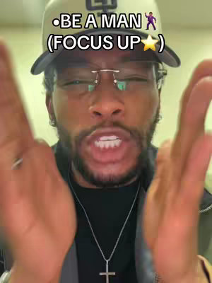A selfie-style video cover image featuring a Black man with short, dark hair and a neatly trimmed beard. He's wearing a tan baseball cap with a logo, small-framed glasses, and a silver cross necklace. The man is looking directly at the camera with an intense expression, his hands outstretched towards the viewer in a gesture as if to grasp or hold something. The background appears to be a plain, light-colored wall. The overall composition is close-up, focusing on the man's face and hands, and the lighting is warm and focused, highlighting his features and creating a sense of direct engagement with the audience.