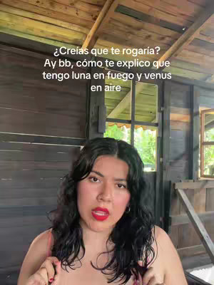 A woman with dark, wavy hair and red lipstick looks directly at the camera. She's positioned indoors in a rustic wooden structure. Text overlays are placed above her head.