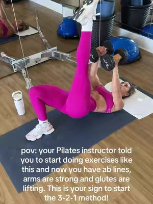 The cover image shows a woman in a gym setting, performing a pilates exercise with dumbbells while lying on a mat. She wears bright pink workout attire, including leggings and a sports bra. The background includes blue and gold exercise equipment. Text overlays provide context and instructions.
