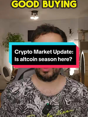 A man in a patterned shirt fills the frame, with a large text box overlay obscuring his mouth. Above him, in large yellow letters, is the phrase 'GOOD BUYING'. The text box promotes the video topic, 'Crypto Market Update: Is altcoin season here?'. The background reveals a room setting, with a plant, lights, and a cat tree. The image is well-lit and appears to be from a vlog or video recording.