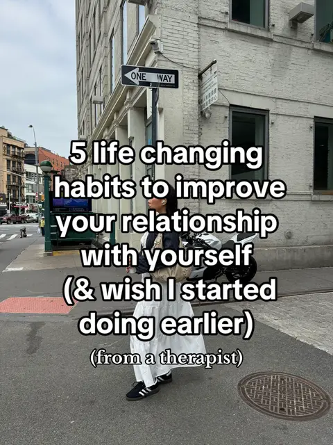 A person is standing on a city street, with a brick building in the background and text overlaid on the image. The text reads "5 life changing habits to improve your relationship with yourself (& wish I started doing earlier) (from a therapist)."