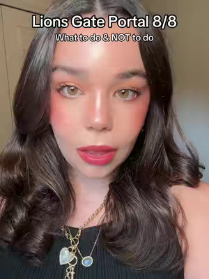A close-up selfie of a woman with long, wavy dark brown hair. She is wearing lip color, blush, and a necklace. Text overlays at the top indicate the video's topic: 'Lions Gate Portal 8/8 What to do & NOT to do'.