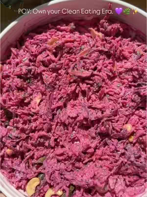 The image shows a close-up shot of a bowl filled with Beetroot Curd Rice. The dish has a vibrant pink color due to the grated beetroot. The texture appears to be a mix of small, shredded pieces and creamy elements, likely from the curd. Some visible ingredients include chopped coriander and cashews. The dish fills nearly the entire frame, with the edge of the bowl visible at the top and bottom. The focus is sharp, highlighting the texture and color saturation of the food.