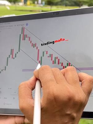 A hand holding a stylus over a tablet displays a stock chart with green and red candlesticks. The chart angles downwards, and lines are drawn to highlight the trend. The background shows blurred green.
