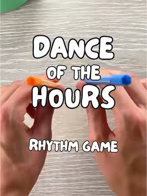 The image shows hands holding a blue and an orange marker with text overlaid that says "DANCE OF THE HOURS RHYTHM GAME"
