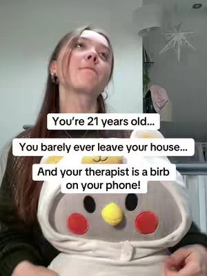 A young woman with light brown hair is looking upward with a questioning expression. She is wearing a dark jacket. Above her is text in white rectangular boxes and a plush bird toy is in front of her.