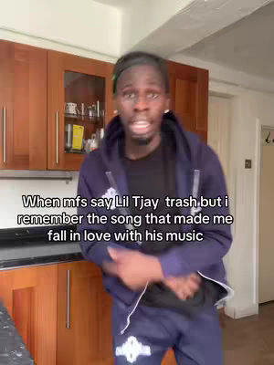A man is standing in a kitchen with dark wooden cabinets and what appears to be a window in the background. The man is wearing a black shirt with a dark blue zip-up hoodie, and he's looking directly at the camera while talking. Text overlay at the bottom of the image. 
