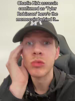 A young man with light skin is the central focus, framed from the chest up. He wears a black baseball cap, a black hoodie, and has a small mustache, a neutral expression. He is touching the side of his face with his hand . Above him, overlayed in black sans-serif text, are the words "Charlie Kirk assassin confirmed as 'Tyler Robinson' here's the memecoin behind it..." against a light background.