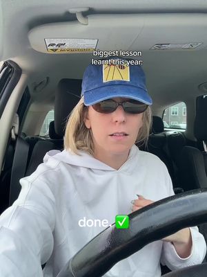 A woman wearing sunglasses and a baseball cap is seated in the driver's seat of a car, facing the camera. Above her head, the words 'biggest lesson learnt this year:' appear as an overlay. The word 'done' with a check mark symbol are also on the bottom left. The scene’s interior is a muted palette, with the car's dashboard and headrest visible in the frame.