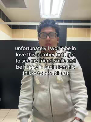 A person wearing glasses and a gray hoodie is centered in a selfie-style shot, set against a neutral background. The person's expression is neutral, and text is overlaid, communicating a message about relationships and October. The composition is straightforward with a focus on the person and the message above.