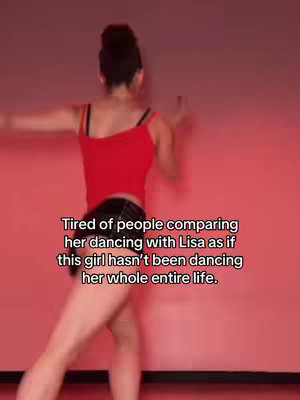 The video cover shows a woman dancing, captured from the back, slightly angled. She’s wearing a red tank top and black shorts, with her hair up. The background is a solid, soft red color. Text overlayed on the image reads, “Tired of people comparing her dancing with Lisa as if this girl hasn’t been dancing her whole entire life.”